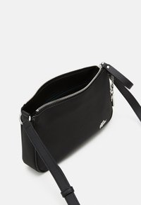 Bolso cruzado sintético negro con cierre de cremallera, diseño plano y correa ajustable. Presenta un acento de logo plateado.