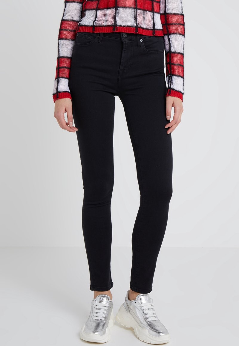 Jeans skinnies negros de denim, con un diseño clásico de cinco bolsillos. Combinados con zapatillas plateadas de suela gruesa y un suéter recortado a cuadros.