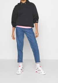 Svart huvtröja med ficka framtill, rosa lager under, blå uppvikta jeans och vita sneakers med grå detaljer.