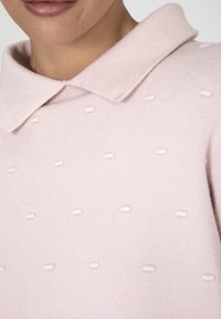 Hellrosa Pullover mit Kragen, der mit gleichmäßig verteilten, strukturierten Punkten auf dem Stoff für zusätzliche Details versehen ist.