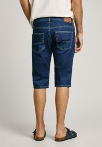 Donkerblauwe denim shorts met een rechte snit, voorzien van twee achterzakken en een leren label op de tailleband. Afgewerkt op knielengte.