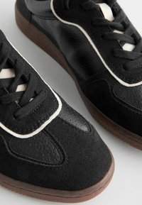 Sneakers neri con un mix di suede testurizzato e pelle liscia, caratterizzati da una rifinitura bianca, lacci neri e una suola in gomma.