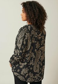Blusa nera con un motivo floreale paisley in oro. Tessuto strutturato con maniche a sbuffo e scollatura rotonda. Design a vestibilità ampia.