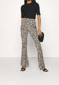 Pantaloni a zampa d'elefante con stampa leopardata, base crema e macchie nere, vita alta; abbinati a un top nero attillato a coste e tacchi neri con cinturini.