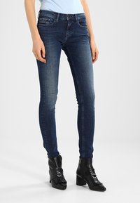 Kapea farkut tummassa pesussa, viidellä taskulla, vyölenkeillä ja hieman haalistuneena. Yhdistetty mustiin nilkkureihin, joissa on hihnat yksityiskohtina.