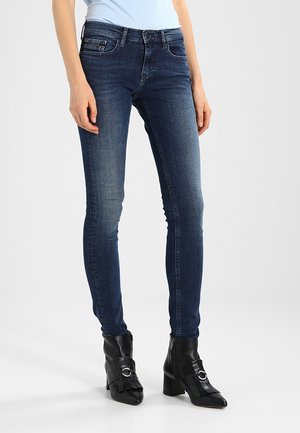 Jeans ajustados en denim de lavado oscuro, que cuentan con cinco bolsillos, pasadores para cinturón y un ligero desgastado. Combinados con botas negras hasta el tobillo con detalles de correas.
