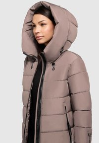 Pufferjack in licht taupe met een grote capuchon, ritssluiting aan de voorkant en zwarte ritszakken aan de zijkant. Gequilt textuur met vulling.
