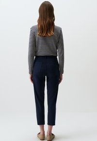 Marineblauwe high-waisted broek met een slim fit, gecombineerd met een cropped gestreept langslavend top. Soepele textuur, minimale detailing en geen zichtbare sluitingen.