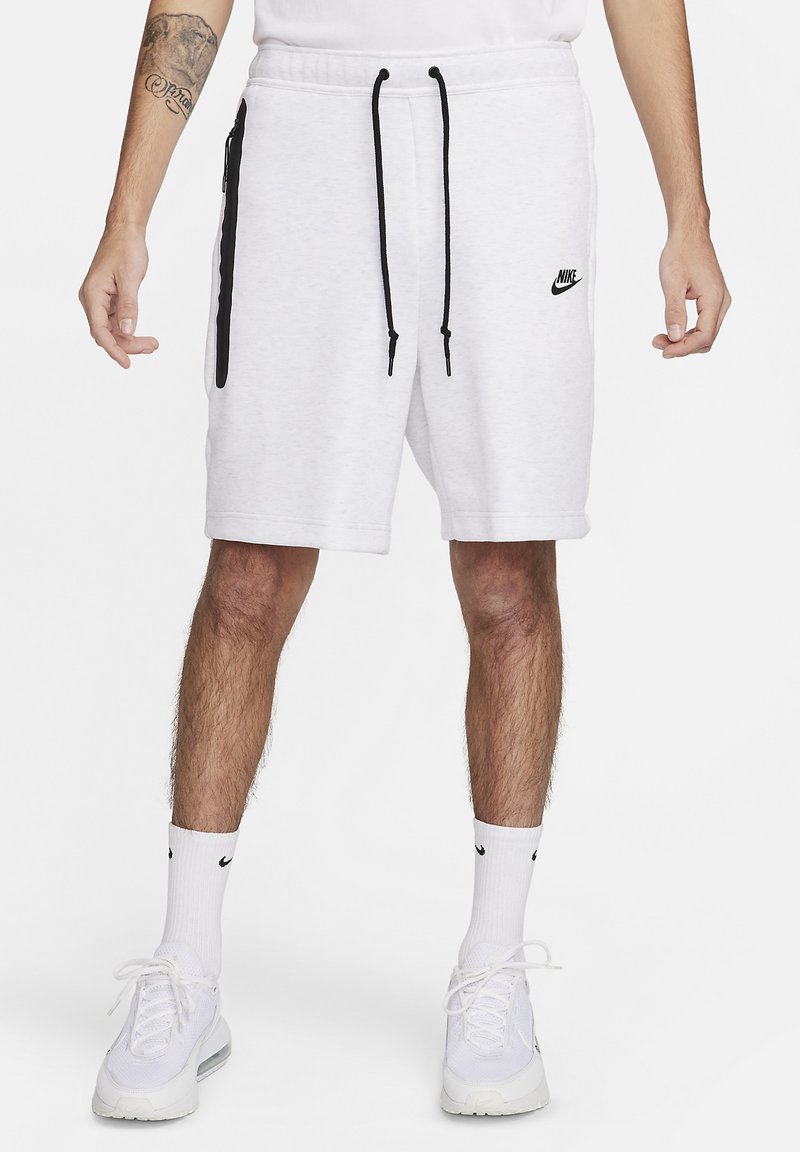 Balti vilnas šorti ar elastīgu jostasvietu un melnām auklām, ar sānu rāvējslēdzēju kabatām un mazu melnu Nike logotipu.