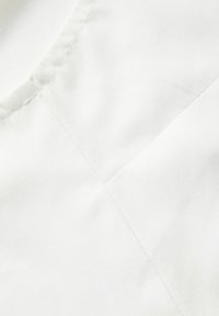 Κοντινή λήψη λευκού υφάσματος με ορατές γραμμές ραφής και λεπτομέρειες ραφής σε μια λεία υφασμάτινη επιφάνεια.