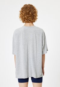 Szary, oversize t-shirt z krótkimi rękawami, okrągłym dekoltem i miękką teksturą. Noszony na granatowych szortach, widok z tyłu.