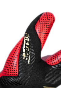 Schwarze und rote Handschuhe mit strukturiertem Griff, gepolsterten Bereichen und goldenen Akzenten. Auffällig sind ihre geometrischen Muster und das ergonomische Design.