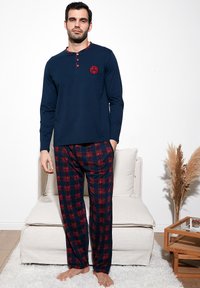 Camisa de manga larga azul marino con cuello y botones de acento rojo, combinada con pantalones de pijama de cuadros rojos y azul marino, que presentan un corte relajado y una tela suave.