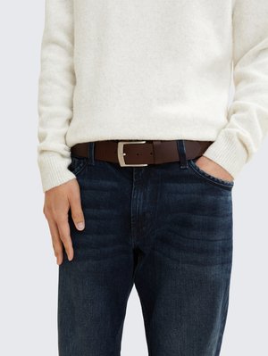 Brun læderbælte med sølvspænde, båret over mørkeblå denimjeans, parret med en lys cremegul striktrøje med ribbenede manchetter.