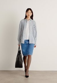 Randig skjorta i blått och vitt, kombinerad med en blå denim blyertskjol. Modellen bär en svart tote-väska och har på sig tunna svarta strumpbyxor och klackar.