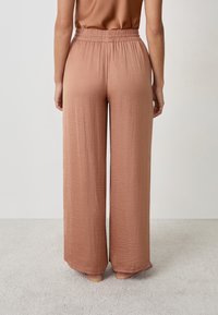 Wijdlopende broek van een zachte, stoffige rozenkleurige stof met een gestructureerd oppervlak en een elastische tailleband. De zoom valt net boven de enkels.