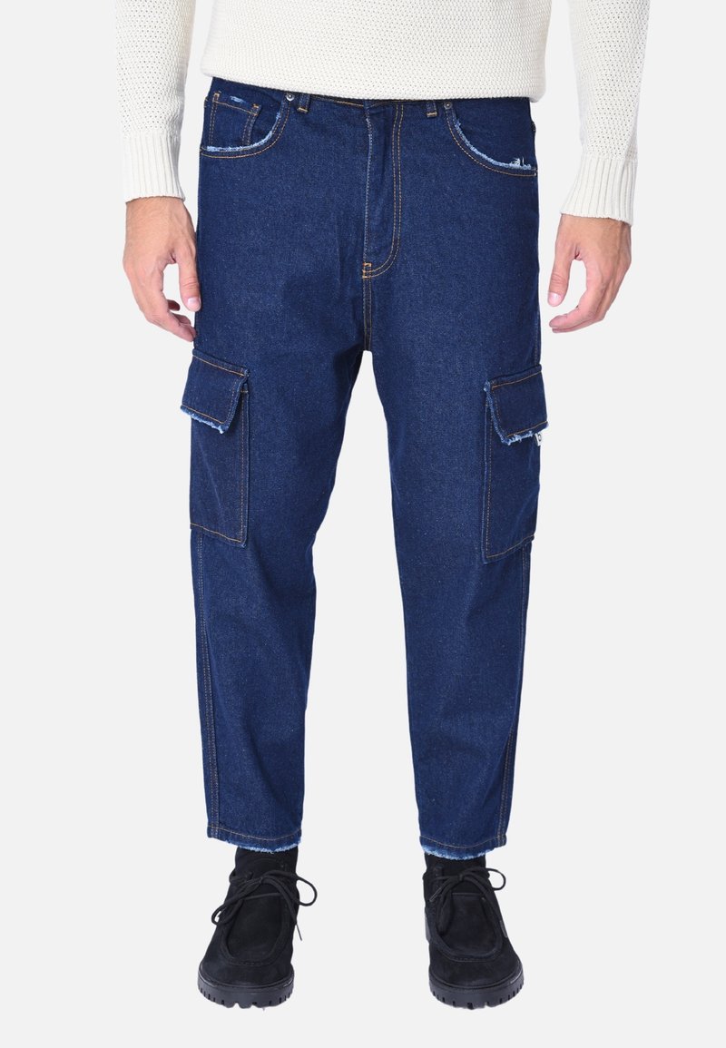Pantaloni cargo in denim blu scuro con due tasche laterali, cuciture a contrasto e vestibilità affusolata. Indossati con scarpe nere stringate.