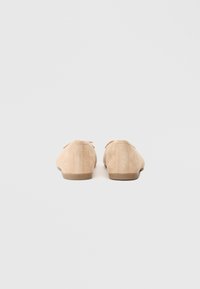 Μπεζ σουέτ παπούτσια με μαλακή υφή, επίπεδες σόλες και διακριτές ραφές, με δέσιμο κορδονιών μπροστά.