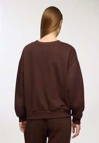 Brązowy, oversize'owy sweatshirt z okrągłym dekoltem i ściągaczami przy rękawach. Miękka tkanina o gładkiej fakturze i luźnym kroju.