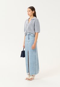 Siva pletena majica s ovratnikom, uparena s svetlo modrim traper maxi krilom s prednjim prorezom in strganim robom. Model drži majhno črno torbico.