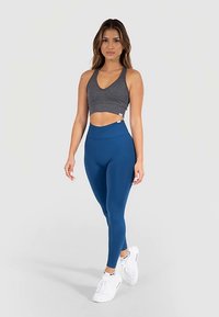 Reggiseno sportivo grigio e leggings blu a vita alta, entrambi realizzati in tessuto elasticizzato, abbinati a scarpe da ginnastica bianche. Design semplice e aderente.