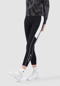 Svarta atletiska tights med vit sidopanel, med en smal passform och en logotyp på nedre benet. Kombineras med en tie-dye sweatshirt och vita sneakers.