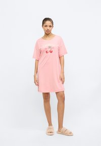 Ροζ νυχτικό με κοντά μανίκια και στρογγυλή λαιμόκοψη, που διαθέτει γραφικό από κεράσια και κείμενο. Φοριέται με μπεζ χνουδωτές παντόφλες.