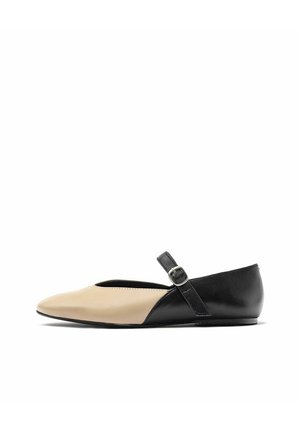 Chaussure plate bicolore avec un bout beige et un talon noir, dotée d'une simple bride cheville avec une boucle, texture en cuir lisse, forme pointue.