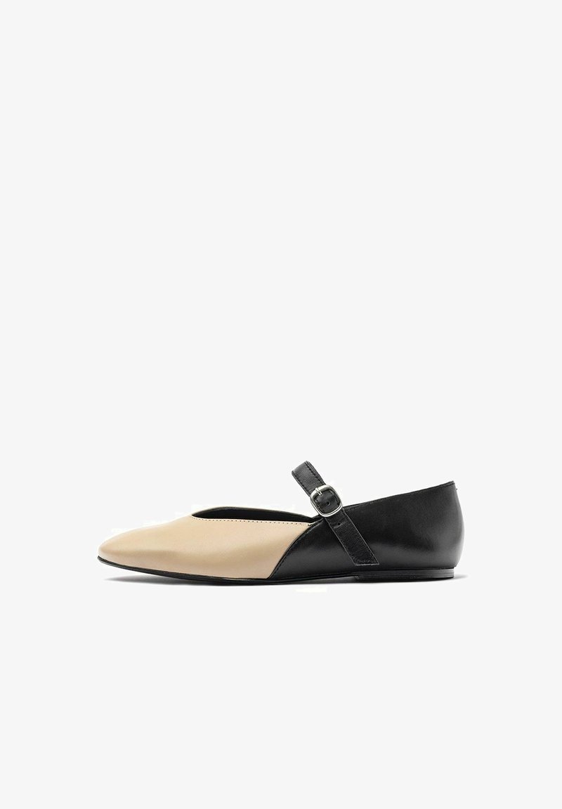 Chaussure plate bicolore avec un bout beige et un talon noir, dotée d'une simple bride cheville avec une boucle, texture en cuir lisse, forme pointue.