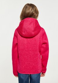 Fuksijos spalvos megztinis su kapišonu, pasižymintis švelniu tekstūru ir šiek tiek marmuriniu išvaizdu. Dizainas apima lenktą apatinę dalį ir ilgomis rankovėmis.