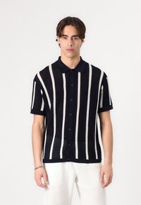 Polo à manches courtes rayé bleu marine et blanc avec un design en maille texturée et des boutons bruns, doté d'un col classique et d'une coupe décontractée.