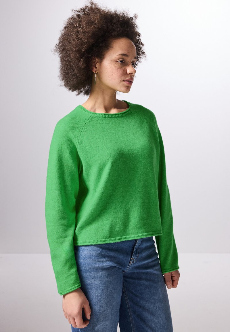 Grön crewneck-tröja i mjukt stickat material. Har långa ärmar och en kort design, kombinerad med ljusblå denimjeans.