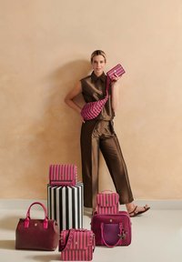 Striped bags in pink and burgundy, featuring various sizes and shapes, on a black and white striped pedestal. Smooth, textured materials.
