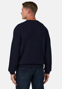 Maglione a maglia blu navy con texture a coste, scollatura rotonda e spalle scese; abbinato a jeans di jeans scuri.
