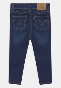 Tmavě modré džíny z denimu s úzkým střihem, vybavené světle hnědou koženou záplatou, dvěma zadními kapsami a kontrastním prošíváním.