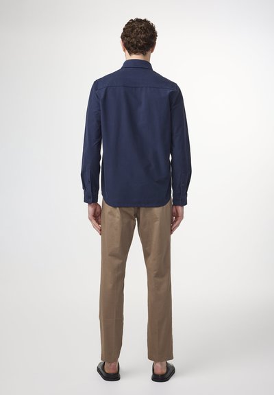 Navy long-sleeve shirt with a straight cut, button cuffs, and a soft texture, paired with beige pants and dark sandals.