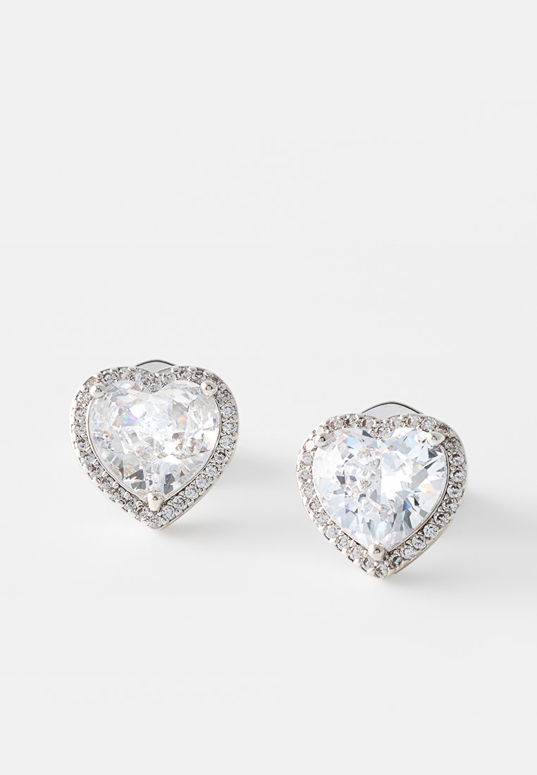 Kolczyki w kształcie serca z dużymi, przezroczystymi kamieniami otoczonymi mniejszymi, błyszczącymi kamieniami. Z tyłu widoczne są metalowe zapięcia.