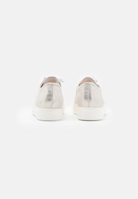 Sneaker metallizzati argento con suola in gomma bianca, dotati di una texture liscia, punta rotonda e lacci frontalmente. La vista posteriore mostra una leggera lucentezza.