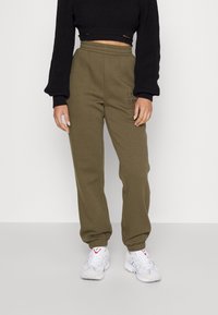 Oliwkowe dresy z elastycznym paskiem i mankietami, z haftowanym napisem. Połączone z białymi butami sportowymi i czarnym dzianinowym topem crop.