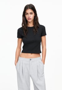 Zwart cropped t-shirt met korte mouwen en een ribbelstructuur, gecombineerd met hoog-getailleerde grijze plooibroek met knoopsluiting.
