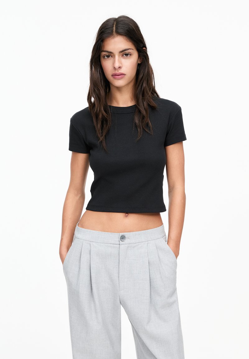 Zwart cropped t-shirt met korte mouwen en een ribbelstructuur, gecombineerd met hoog-getailleerde grijze plooibroek met knoopsluiting.