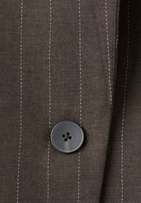 Povečan posnetek temno rjave tkanine z navpičnimi črtami z mat črnim štiri luknjastim gumbom, prišit na tkanino.