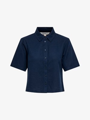 Tumesinine lühikeste varrukatega nööpidega pluus teravate kraeotsadega, lühendatud pikkusega ja külje siseküljel nähtava brändi sildiga.