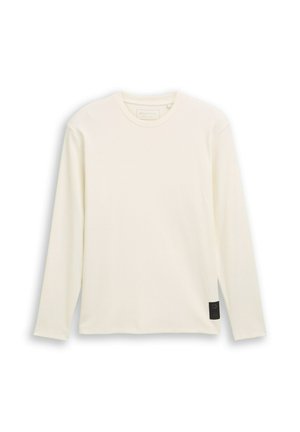 Langærmet, cremefarvet T-shirt lavet af ribbet stof. Har en rund halsudskæring og en lille sort mærkeaccent på siden.