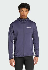 Veste à capuche bleue marine avec zip complet, marquée "TERREX" sur la poitrine, dotée d'une poche avant et d'un tissu texturé pour plus de chaleur.