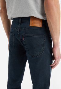 Mörkblå denimjeans med en läderbaksdekal, femficksdesign och väldefinierad sömnad på bakfickorna.