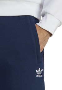 Navyblaue Jogginghosen aus einem weichen Baumwollgemisch mit Seitentaschen; mit weißem gesticktem Adidas-Trefoil-Logo am Oberschenkel.