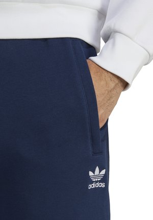 Pantalons de survêtement bleu marine en mélange de coton doux avec poches latérales ; présente le logo tréfle blanc brodé d'Adidas sur la cuisse.