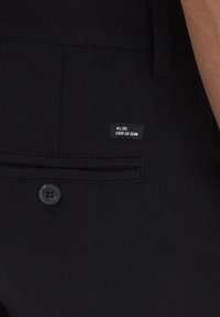 Črne jeans hlače z sprednjo žepek in gumbnim zapiranjem, s oznako "VSAK DAN, CELO DNEVNO JEANS." Gladka tekstura, prilegajoč kroj.