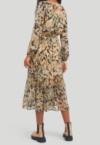 Lång, genomskinlig klänning i ett camouflage-mönster med nyanser av grönt, brunt och persika. Har långa ärmar, resårmidja och lager av fåll.